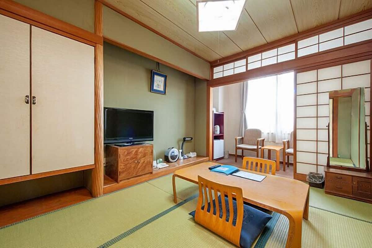 A traditional Japanese room with tatami flooring, a television, a cabinet, and a dining table with chairs.