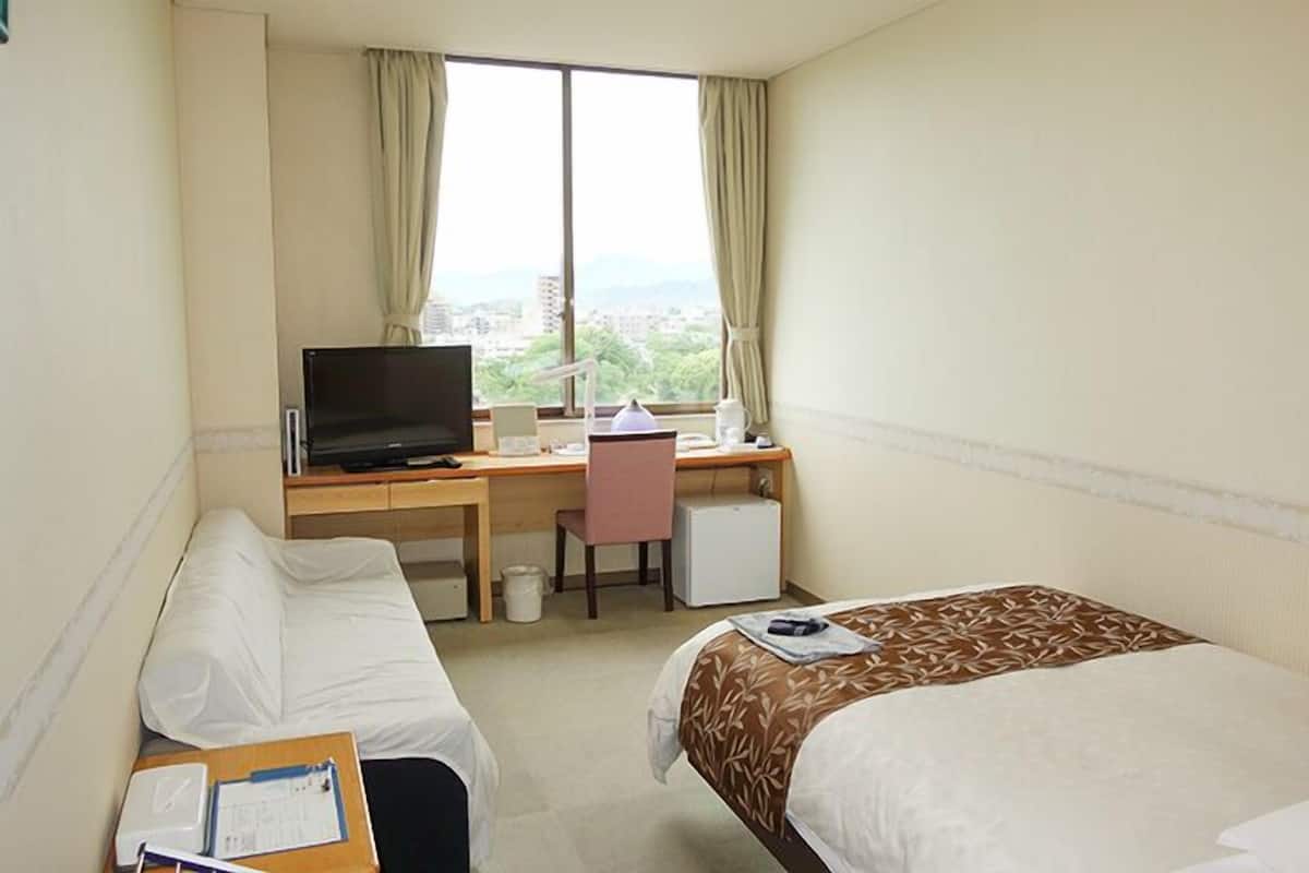 Une chambre d’hôtel avec deux lits, un bureau avec un ordinateur, une télévision et une fenêtre avec des rideaux.
