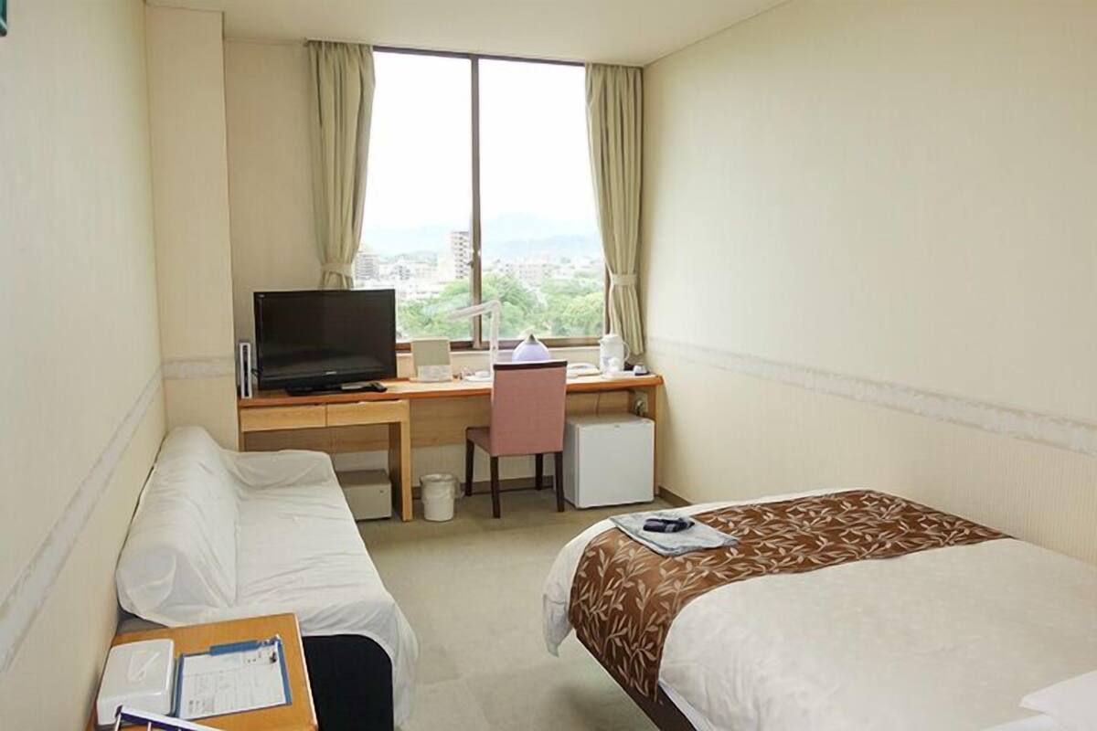A hotel room with two beds, a desk with a computer, a television, and a window with curtains.