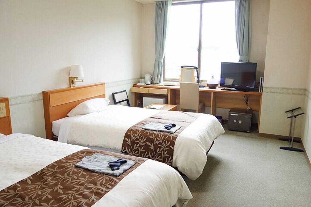 Une chambre d’hôtel avec deux lits, un bureau, une télévision et une fenêtre avec des rideaux.