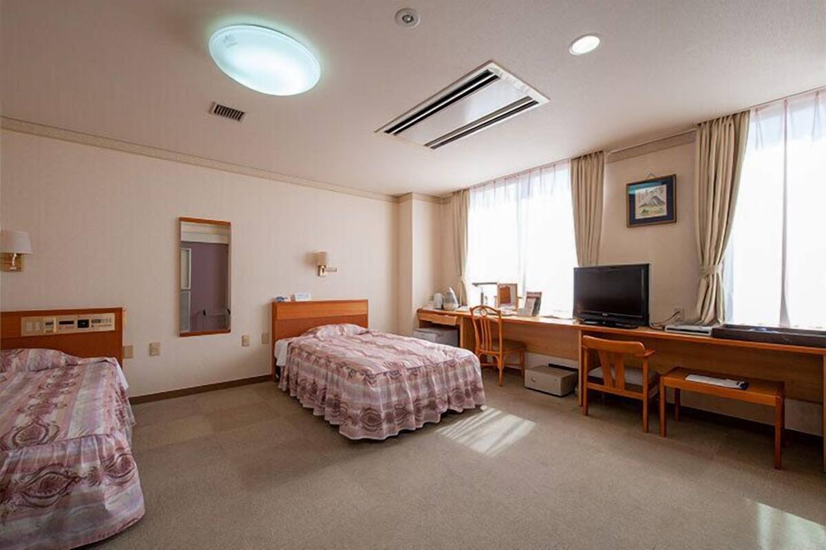 Une chambre d’hôtel avec deux lits, un bureau avec un ordinateur, une télévision et une fenêtre avec des rideaux.