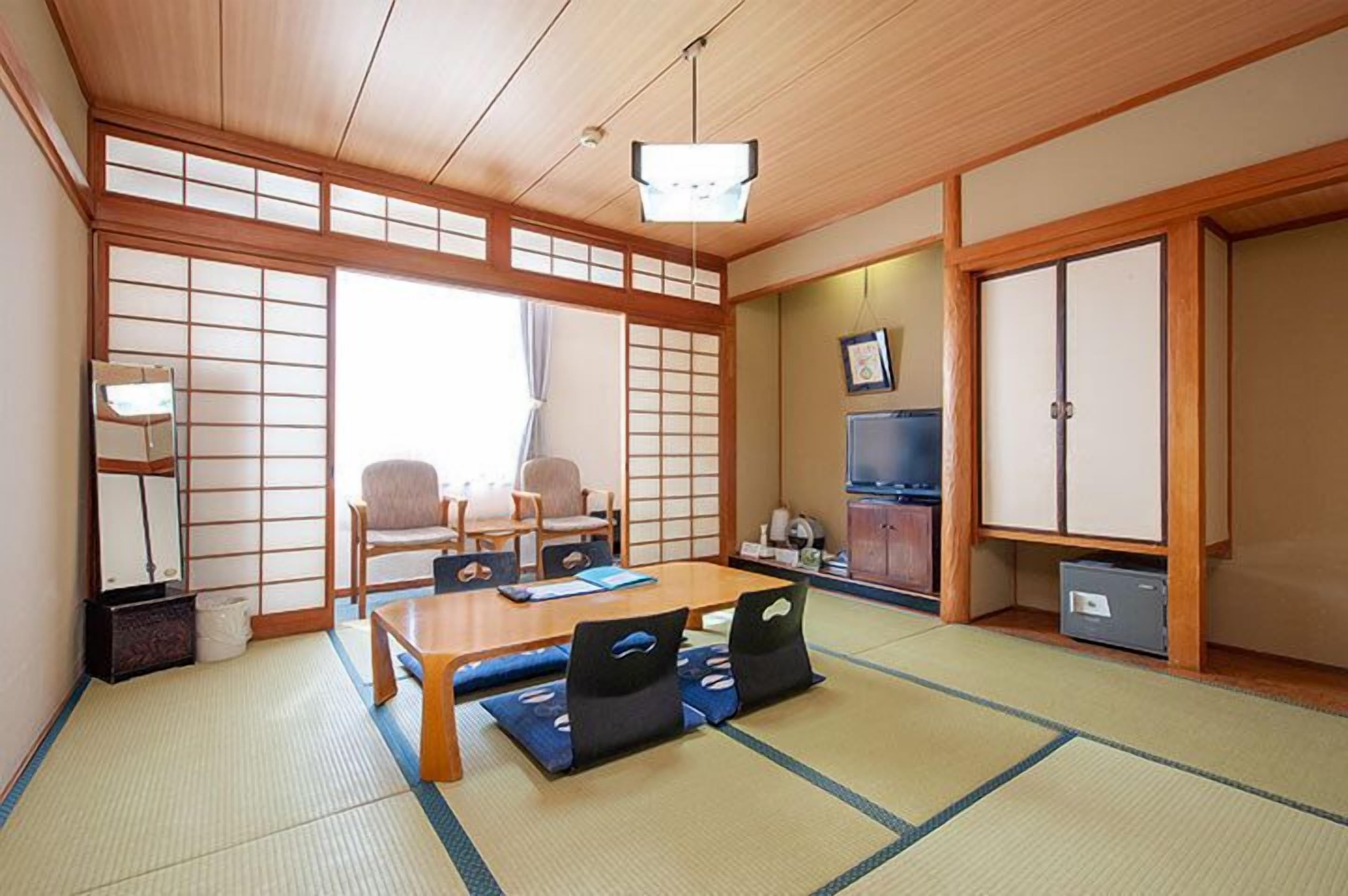 A traditional Japanese room with tatami flooring, a low table with cushions, a television, and sliding doors.