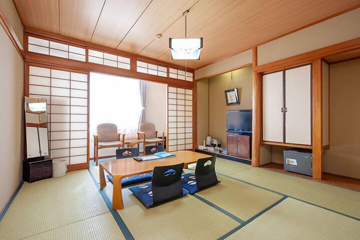 Une pièce de style japonais traditionnel, avec un sol recouvert de tatamis, une table basse avec des coussins, un téléviseur et des portes coulissantes.