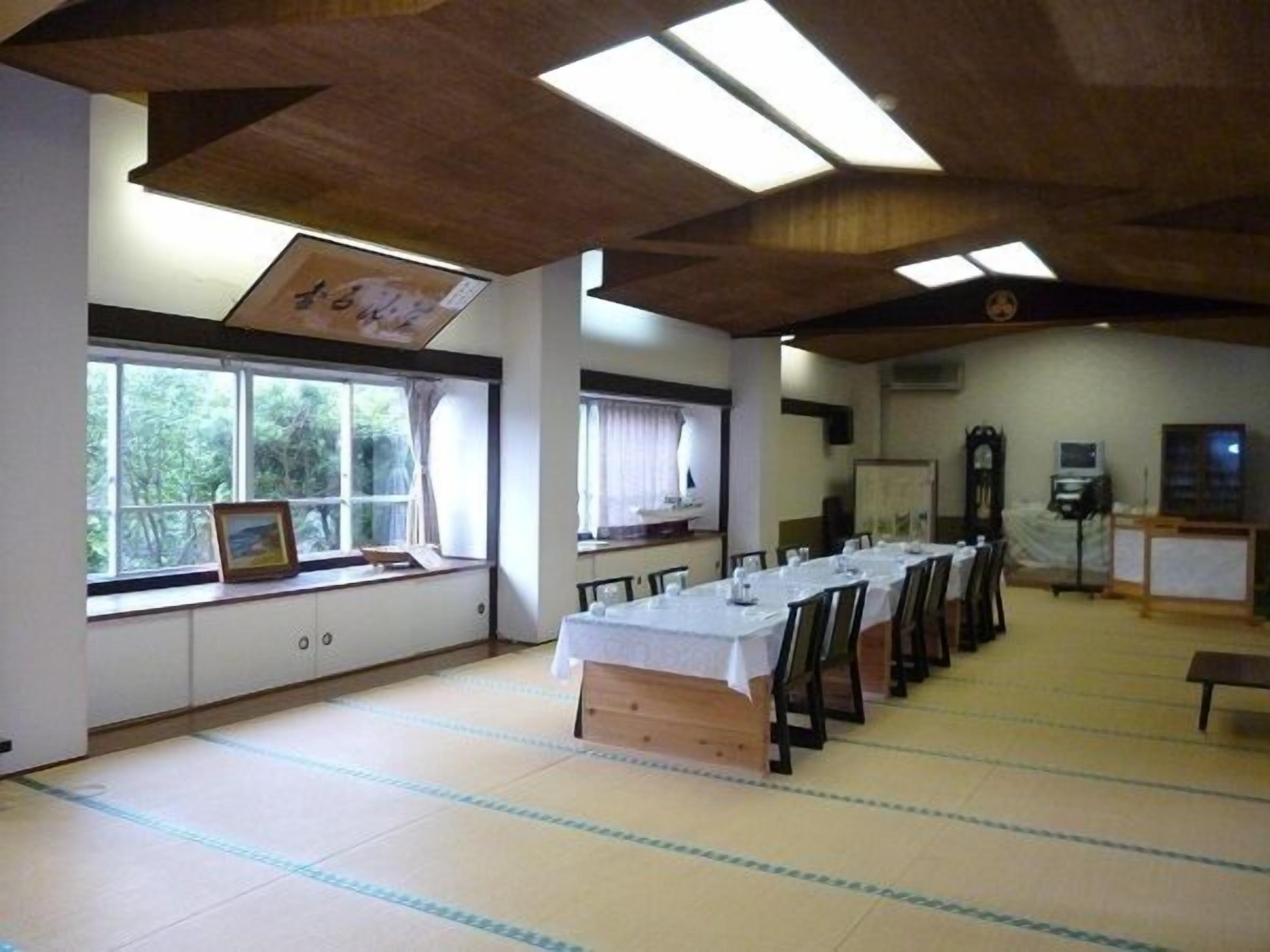 A room with a long table set for dining, large windows, and a wooden ceiling.