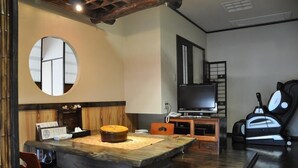 Ein traditioneller japanischer Wohnraum mit Tatami-Böden, einem niedrigen Holztisch, einem Fernseher und einer Futon-Liegefläche.