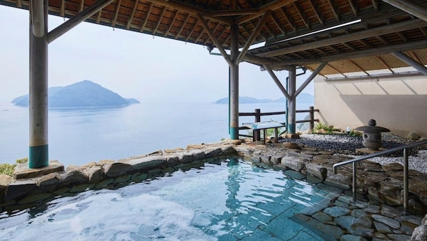 Una piscina in pietra con un pontile di legno e vista su un'isola in lontananza.