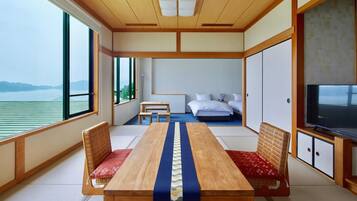 Quarto com mesa de madeira, duas cadeiras, uma cama, televisão e vista para o mar.