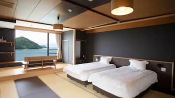 Quarto de hotel com uma janela grande, duas camas, um banquinho e vista para o mar.