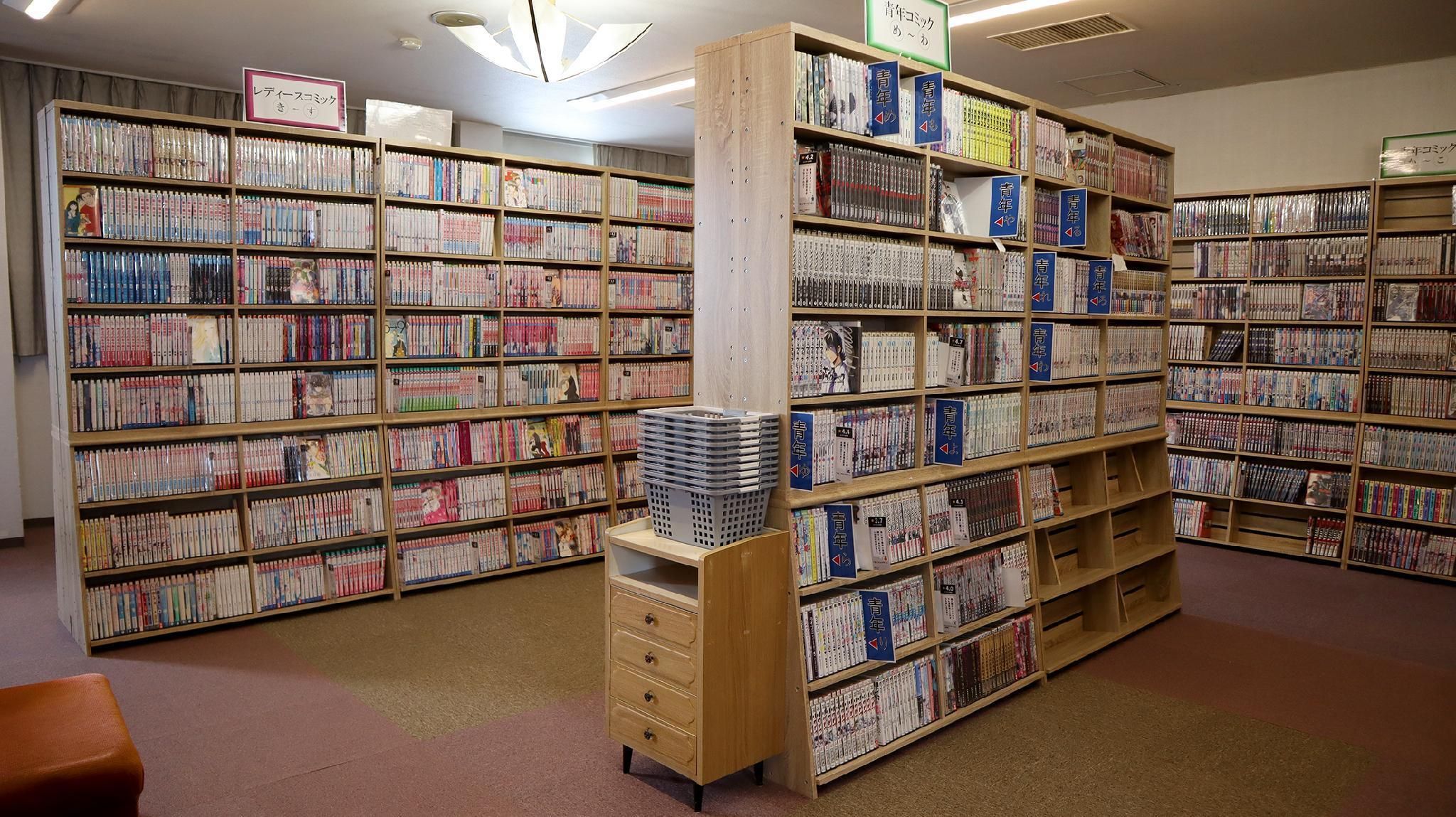 Une bibliothèque avec de nombreuses étagères remplies de livres. Des panneaux indiquent les différentes sections.