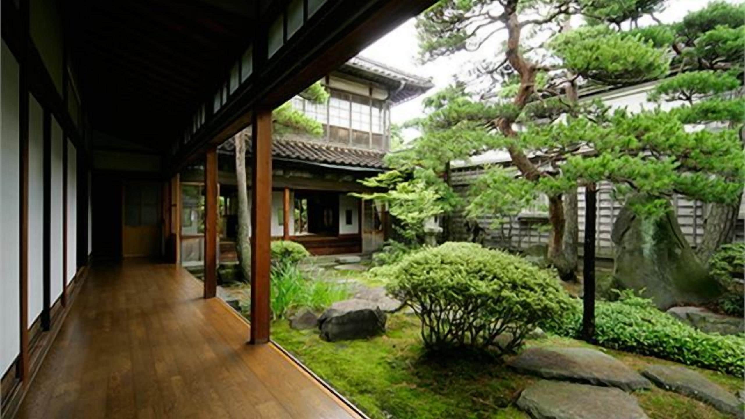 Un edificio japonés tradicional con un corredor de madera que conduce a un jardín con rocas y árboles.