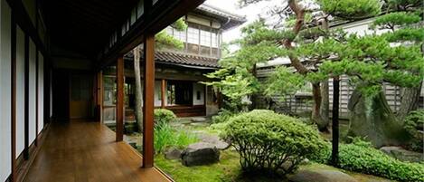 Ein traditionelles japanisches Gebäude mit einem hölzernen Gang, der zu einem Garten mit Steinen und Bäumen führt.