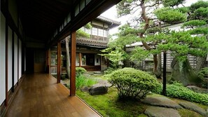 Un edificio tradizionale giapponese con un portico in legno che conduce a un giardino con rocce e alberi.