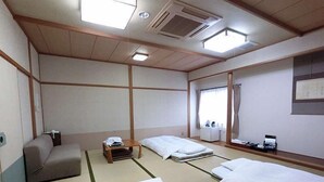 Habitación de hotel de estilo japonés tradicional, con suelo de tatami, una cama de madera baja, un pequeño sofá y un escritorio con una silla.