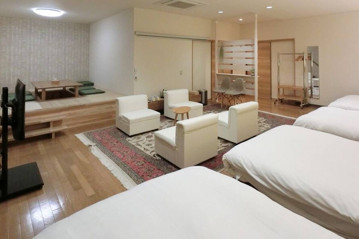 A hotel room with a bed, a desk, a chair, a small table, a TV, and a wardrobe.