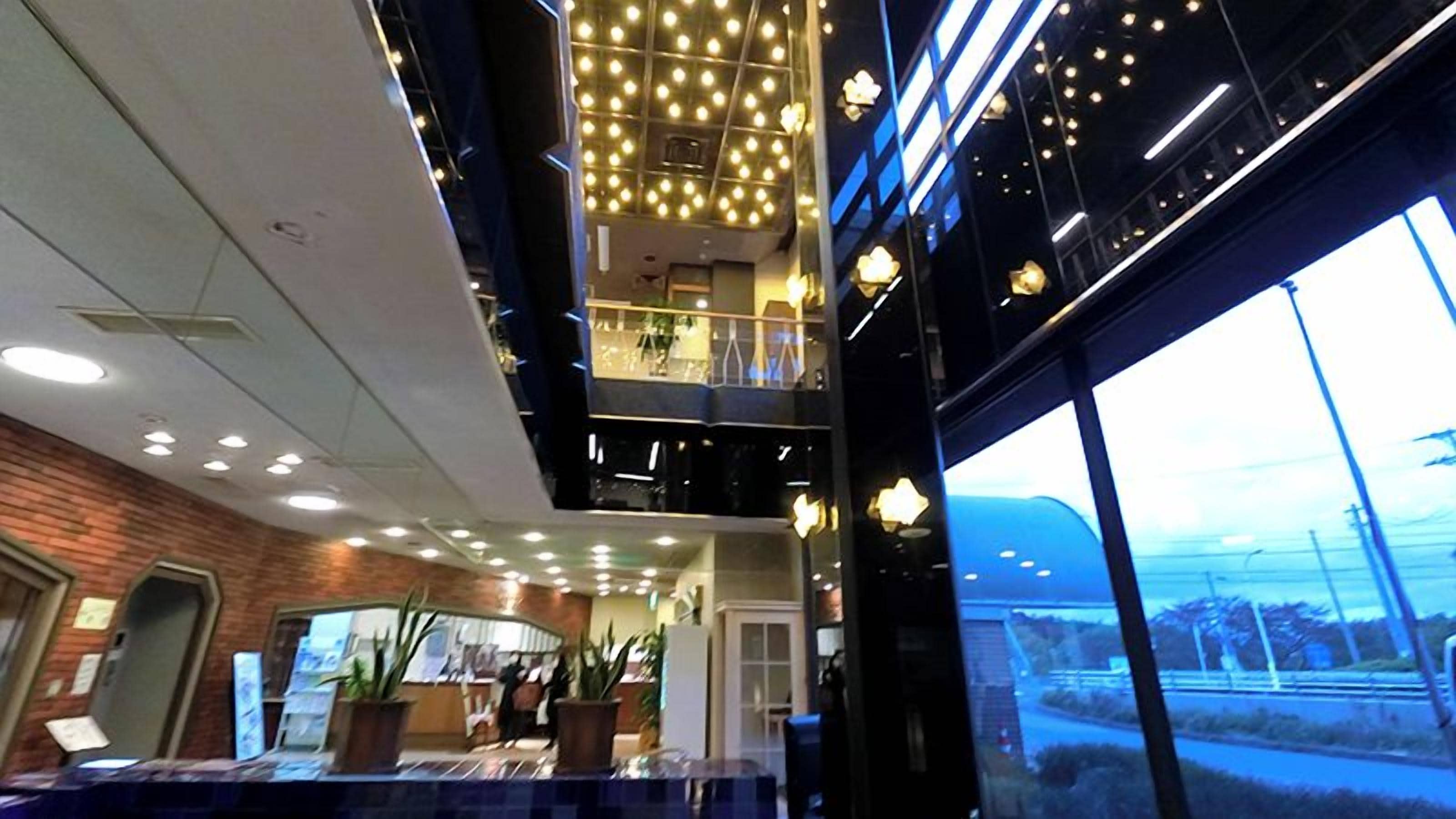 Vestíbulo de hotel con diseño moderno, que presenta un amplio ventanal, una pared de ladrillo y un techo con luces colgantes.