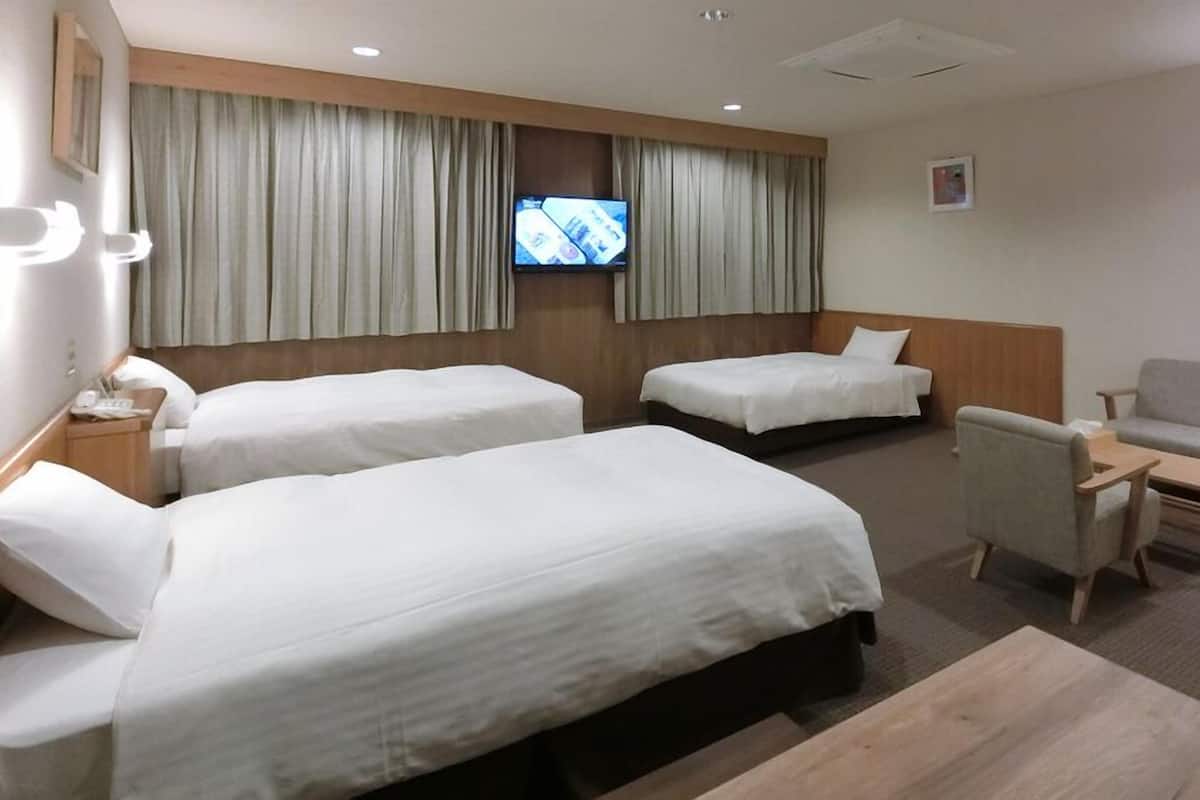 A hotel room with two beds, a TV, a sofa, and a small table.
