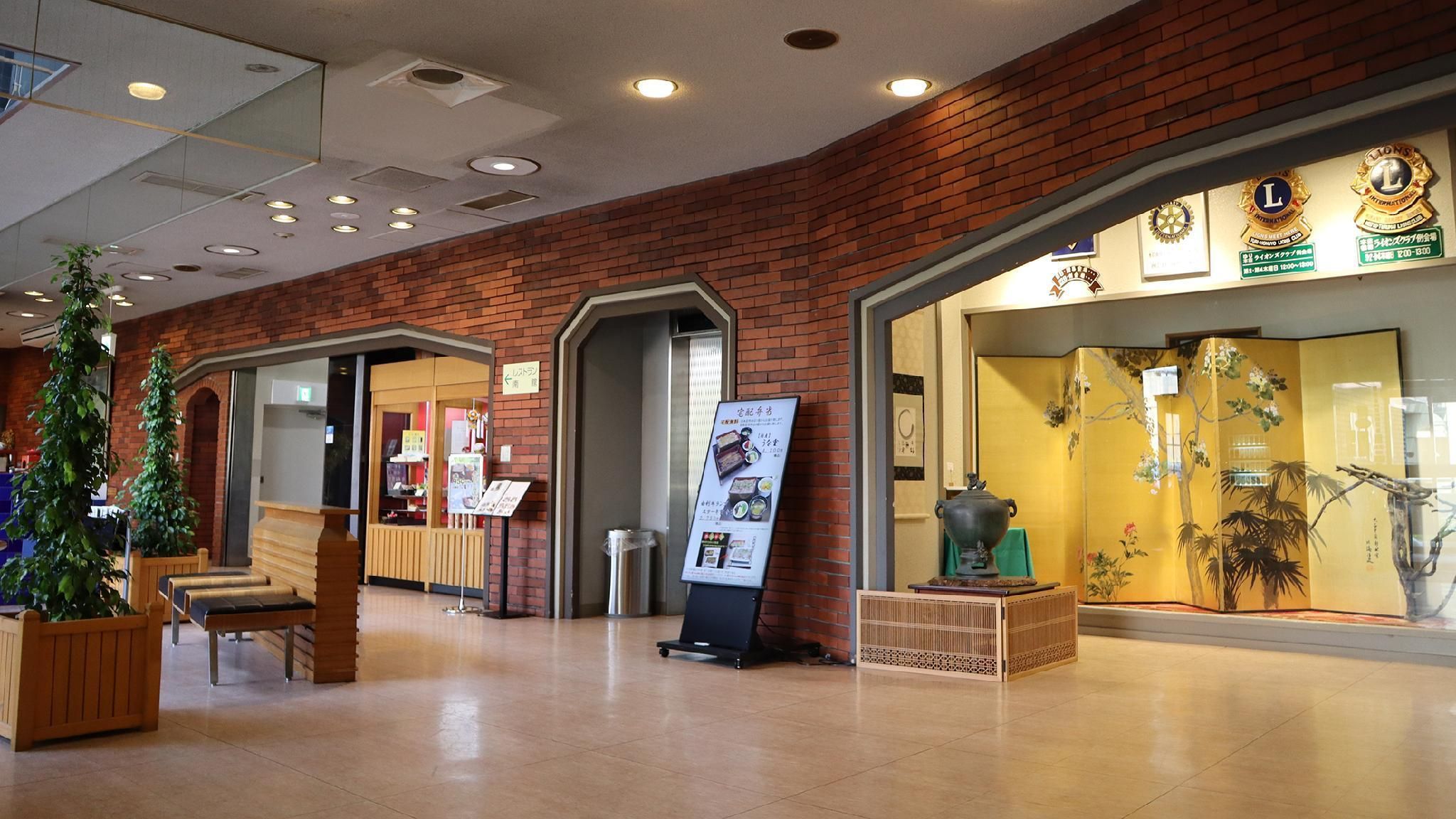 A lobby with a brick wall, a reception desk, a seating area with benches, a display board, and a traditional Japanese screen.