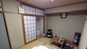 Una habitación tradicional japonesa con suelo de tatami, una cama, un televisor y una pequeña mesa.