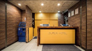 A reception desk with a 'Super Hotel' sign, a blue self-service kiosk, and wooden paneling on the walls. - Super Hotel Yokkaichi Kokudoichigozoi (Yokkaichi)