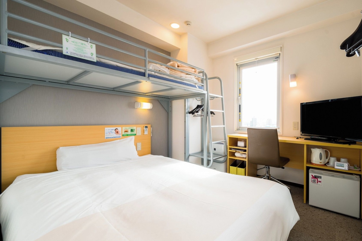 A hotel room with bunk beds, a desk with a TV, and a small kitchenette.