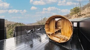 A wooden sauna structure with benches inside, situated on a wooden deck with a view of a mountainous landscape. - Glamping Spa Waita (Oguni)