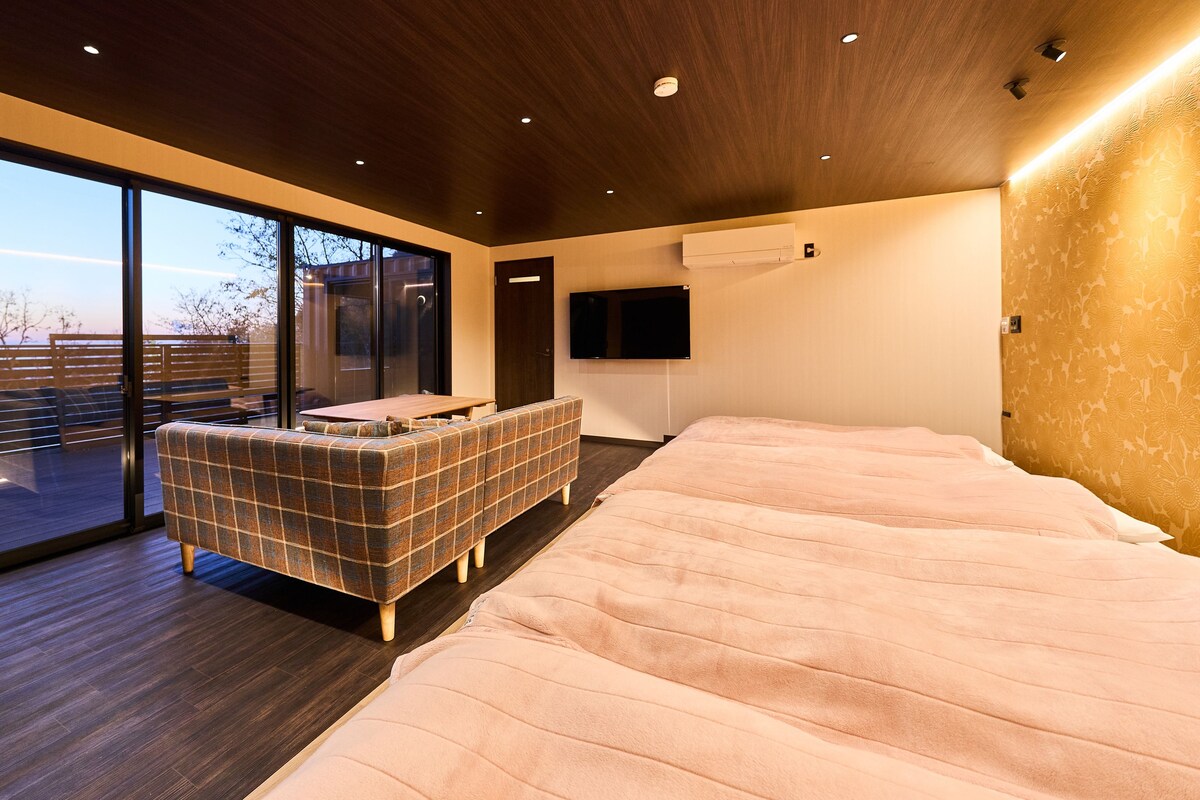A modern bedroom with a large bed, a sofa, and a sliding glass door leading to a balcony.