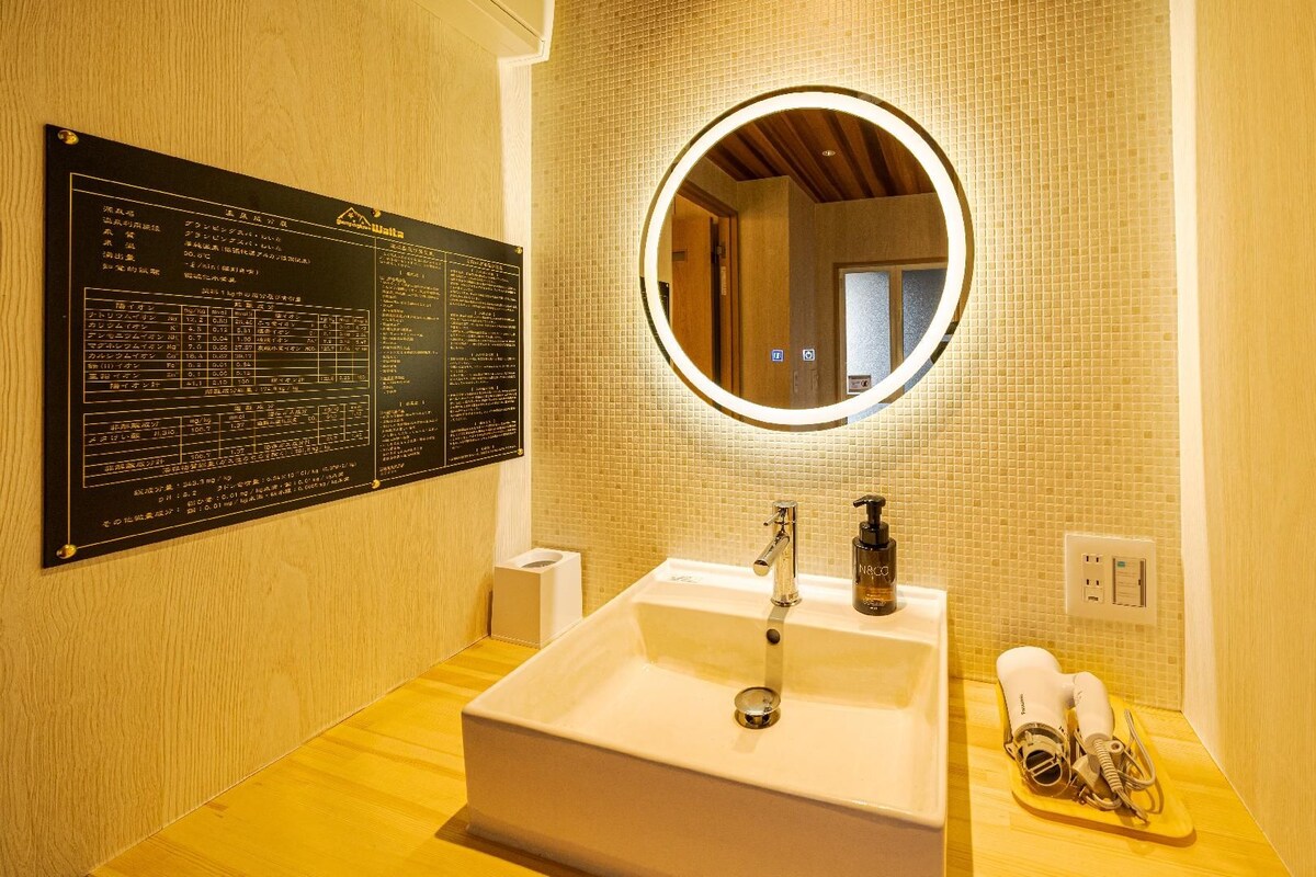 A bathroom with a white sink, a mirror with a light, a towel rack, and a wall-mounted information board.