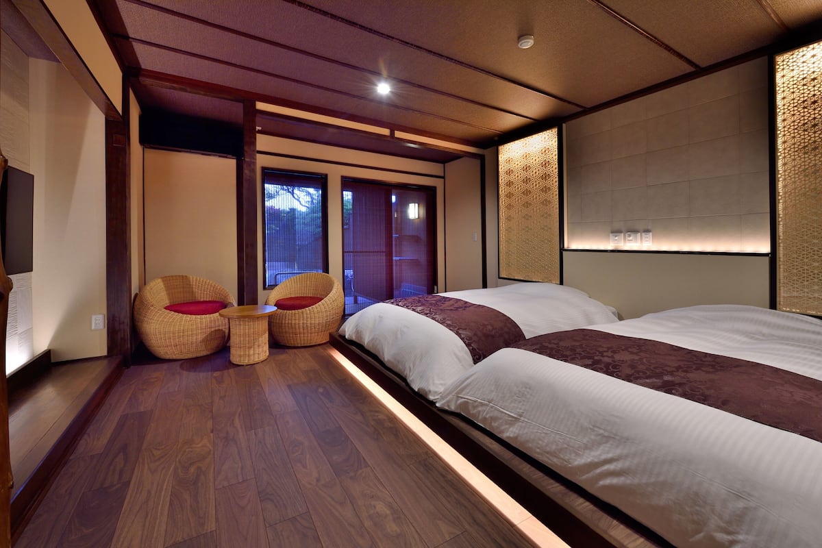 Een hotelkamer met een bed, twee stoelen, een tafeltje, houten vloeren en schuifdeuren.