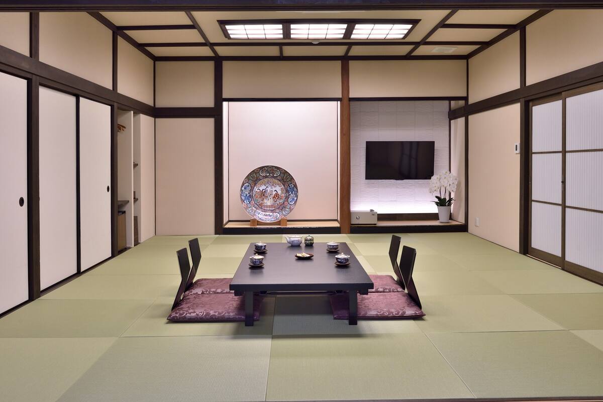 Une pièce de style japonais traditionnel, avec un sol recouvert de tatamis, une petite table basse sur laquelle sont disposés des accessoires pour la cérémonie du thé, des portes coulissantes et un téléviseur.