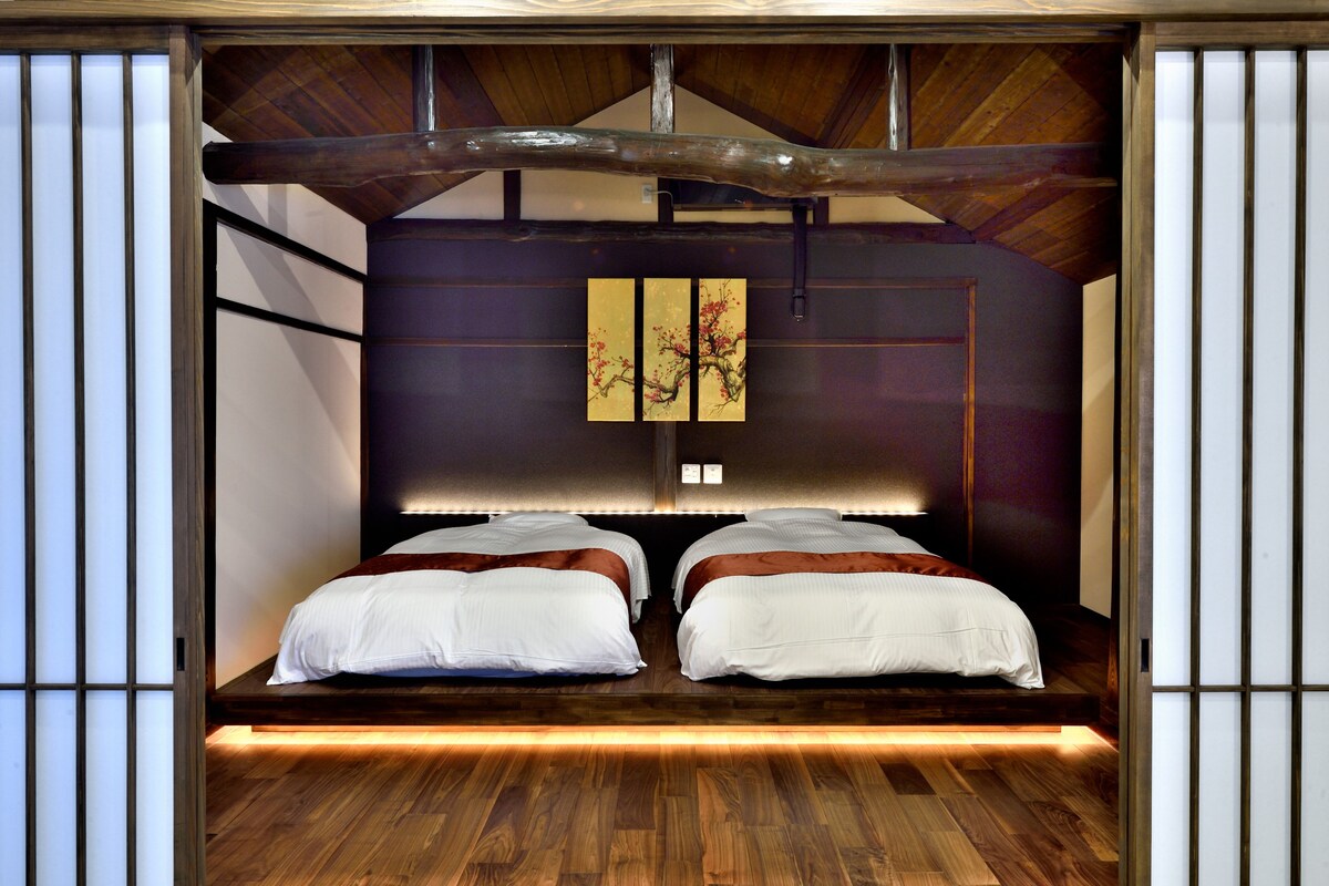 A room with a wooden ceiling, two beds with white bedding, a wall-mounted artwork, and a wooden floor.