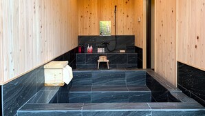Un interior de madera con un lavabo de mármol negro, escalones de madera y un pequeño taburete de madera.