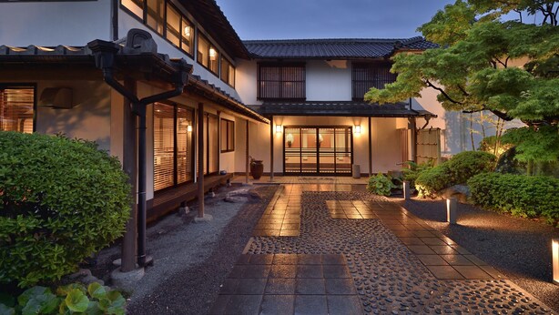 Una casa japonesa tradicional con un acceso de tejas, un banco de madera y un jardín bien cuidado.