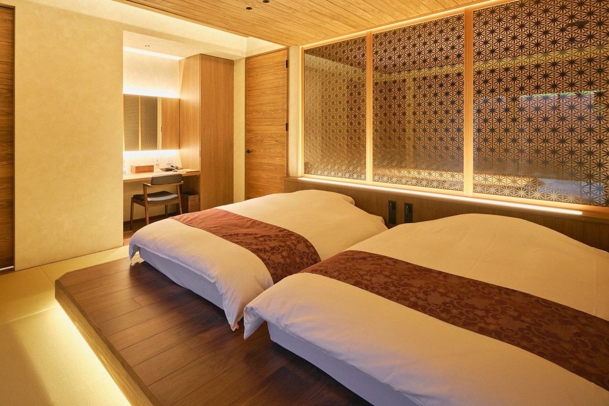 A hotel room with a wooden floor, a desk with a chair, and a bed with patterned bedding.