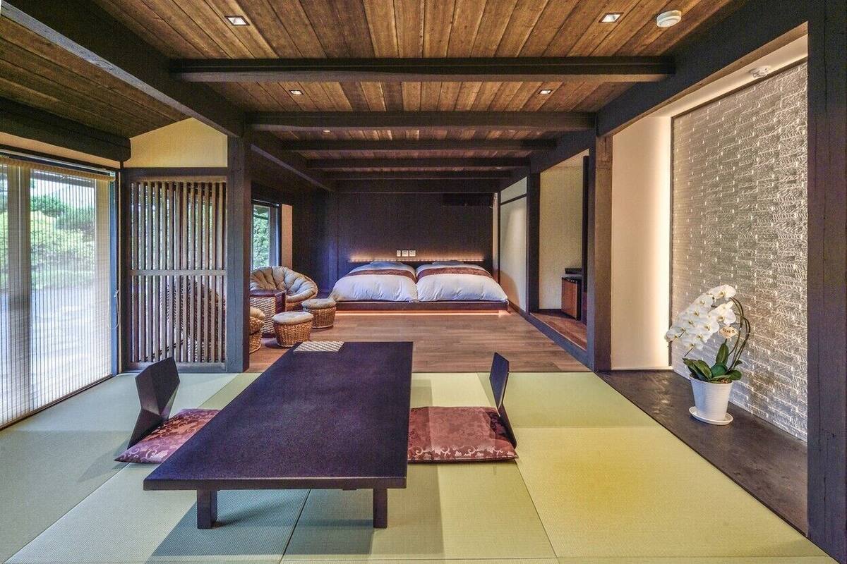 Une pièce de style japonais traditionnel, avec un sol recouvert de tatamis, un plafond bas en bois et un lit avec une literie blanche.