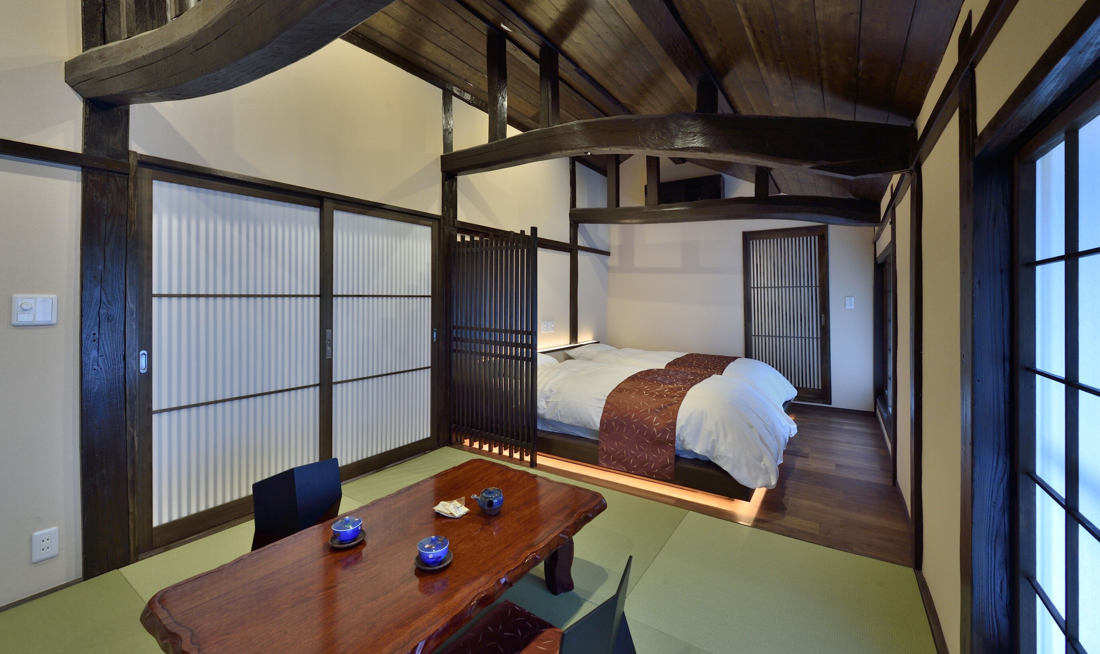 Una habitación japonesa tradicional con suelo de tatami, una cama de madera baja y un panel corredizo shoji.