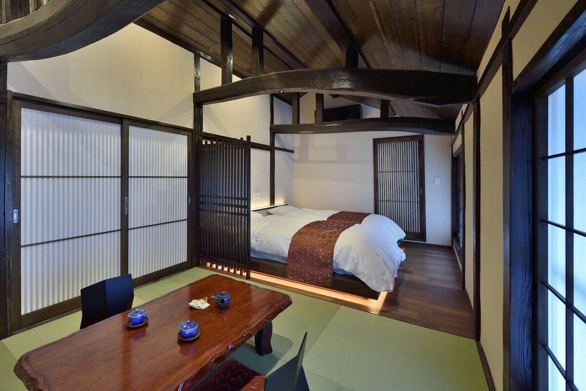 Une pièce de style japonais traditionnel, avec un sol recouvert de tatamis, un lit bas en bois, des portes coulissantes en papier de riz (shoji) et une table avec un service à thé.