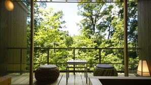 A wooden deck with a table and two stools, overlooking a lush green forest. - Spa Terrace Shisui (Kobe)