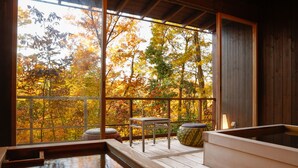A wooden deck with a hot tub, a small table, and a bench, overlooking a forest with autumn foliage. - Spa Terrace Shisui (Kobe)