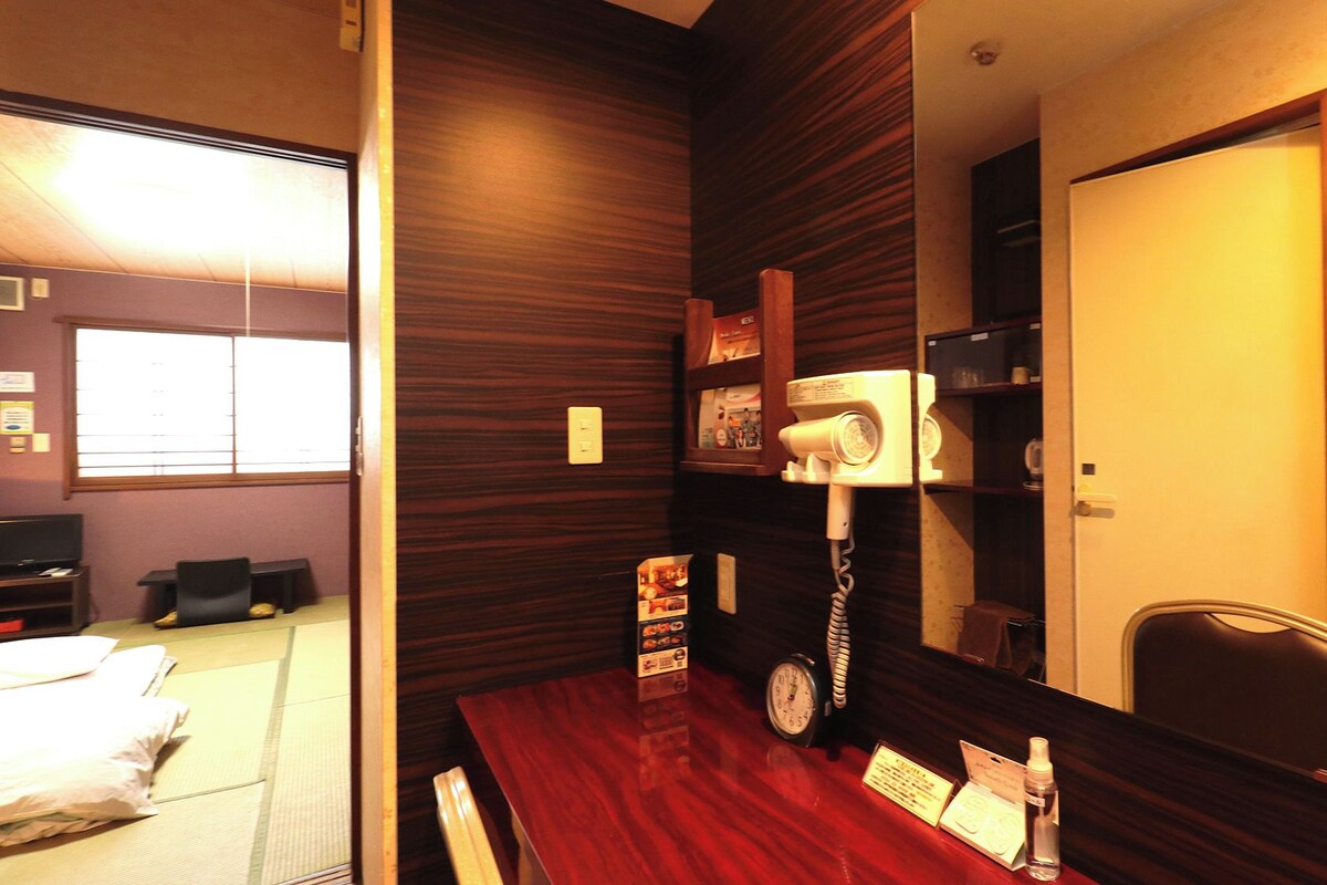 A hotel room with a wooden wall, a desk with a telephone, a clock, and a mirror.