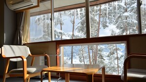 A room with a large window offering a view of snow-covered trees. There are two wooden chairs and a small table.