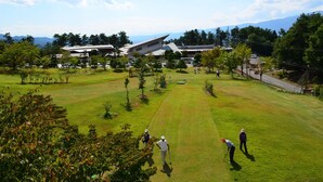 A golf course with a clubhouse, a parking area, and a mountainous backdrop.