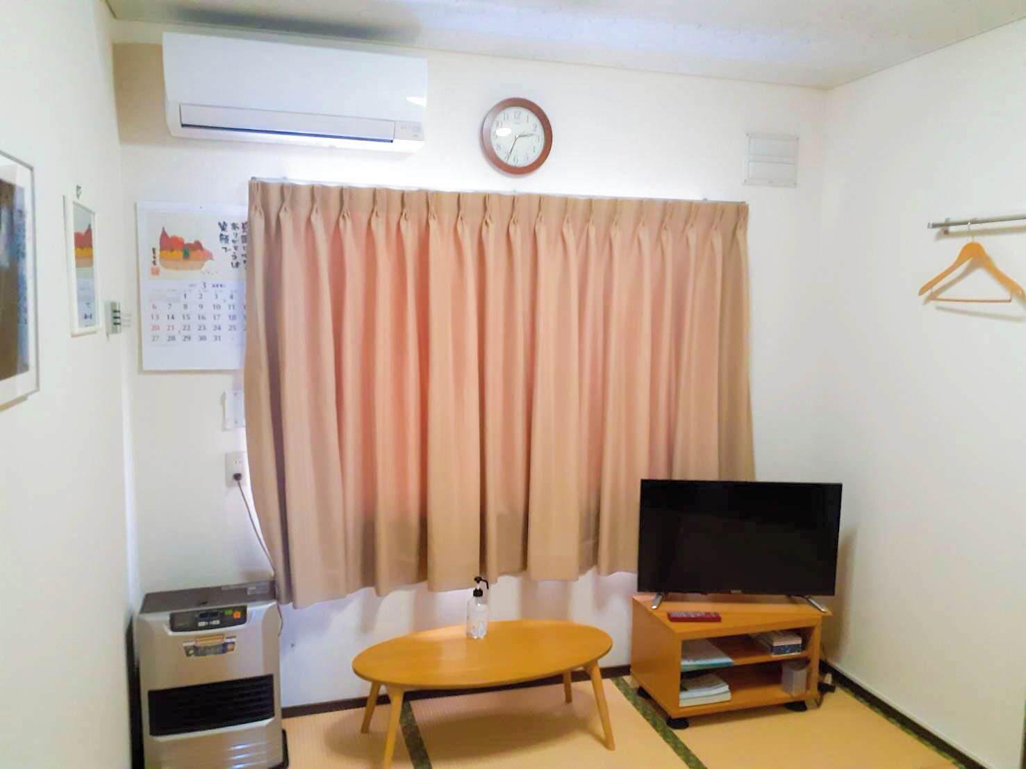 Ein Wohnzimmer mit Flachbildfernseher, einem kleinen Tisch, einer Couch, einer Klimaanlage, einer Uhr und einem Kalender.