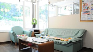 Une pièce avec un canapé vert clair, un fauteuil assorti, une table basse en bois sur laquelle se trouvent des papiers et un panier, ainsi qu’une plante en pot.