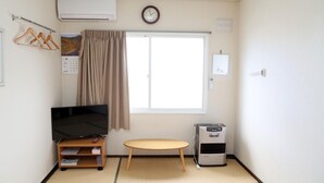 Une pièce comprenant un téléviseur posé sur un meuble, une petite table, un radiateur, une fenêtre avec des rideaux, une horloge murale et un calendrier.
