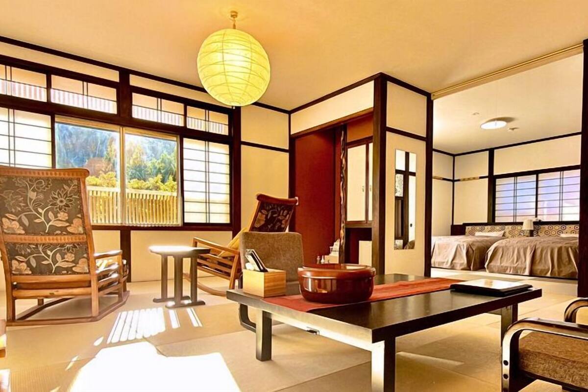 Um quarto tradicional japonês com tatames, uma mesa baixa, um sofá e uma cama.