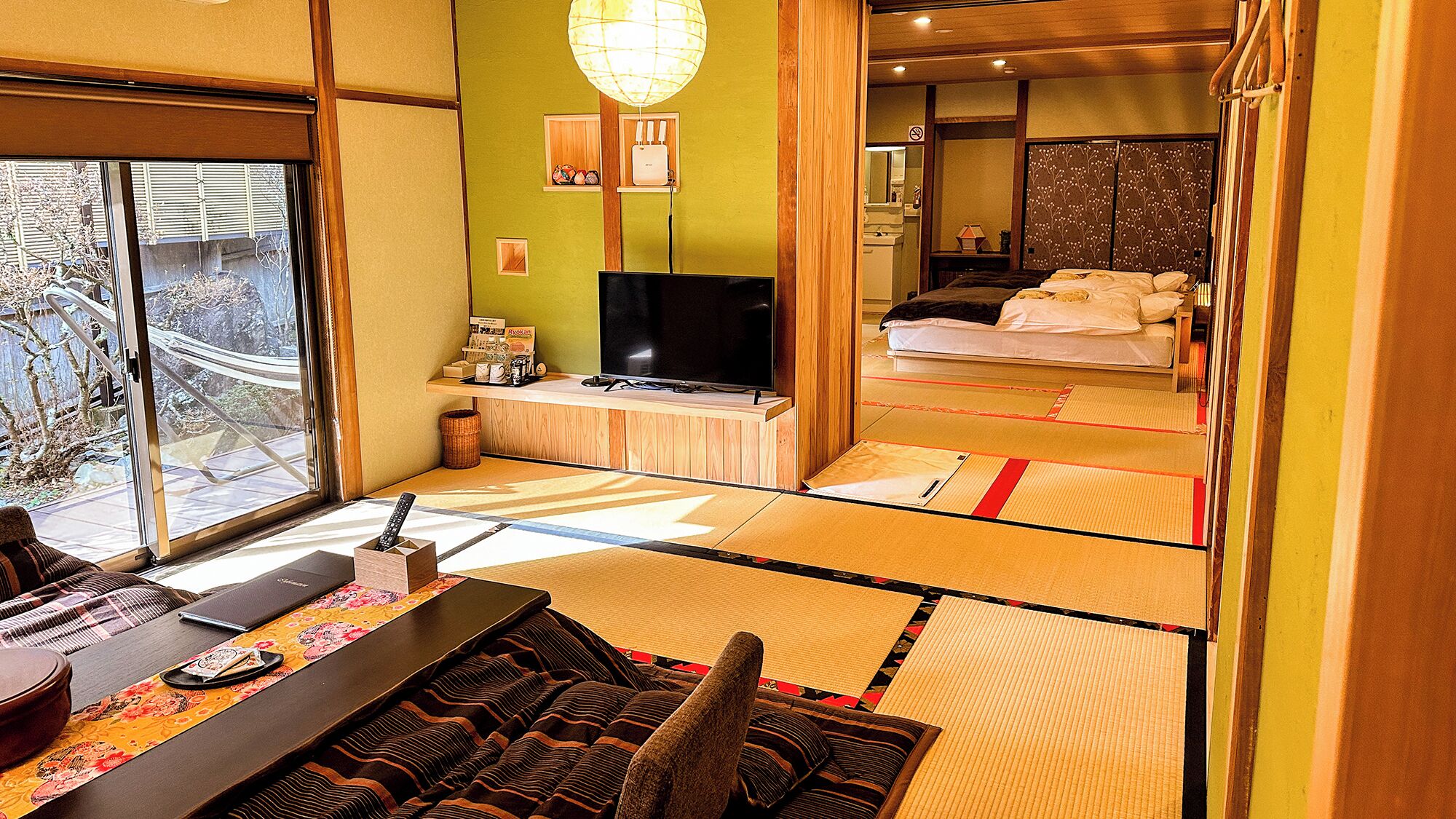 Une pièce de style japonais traditionnel, avec un sol recouvert de tatamis, une télévision, un lit et une vue sur l’extérieur.