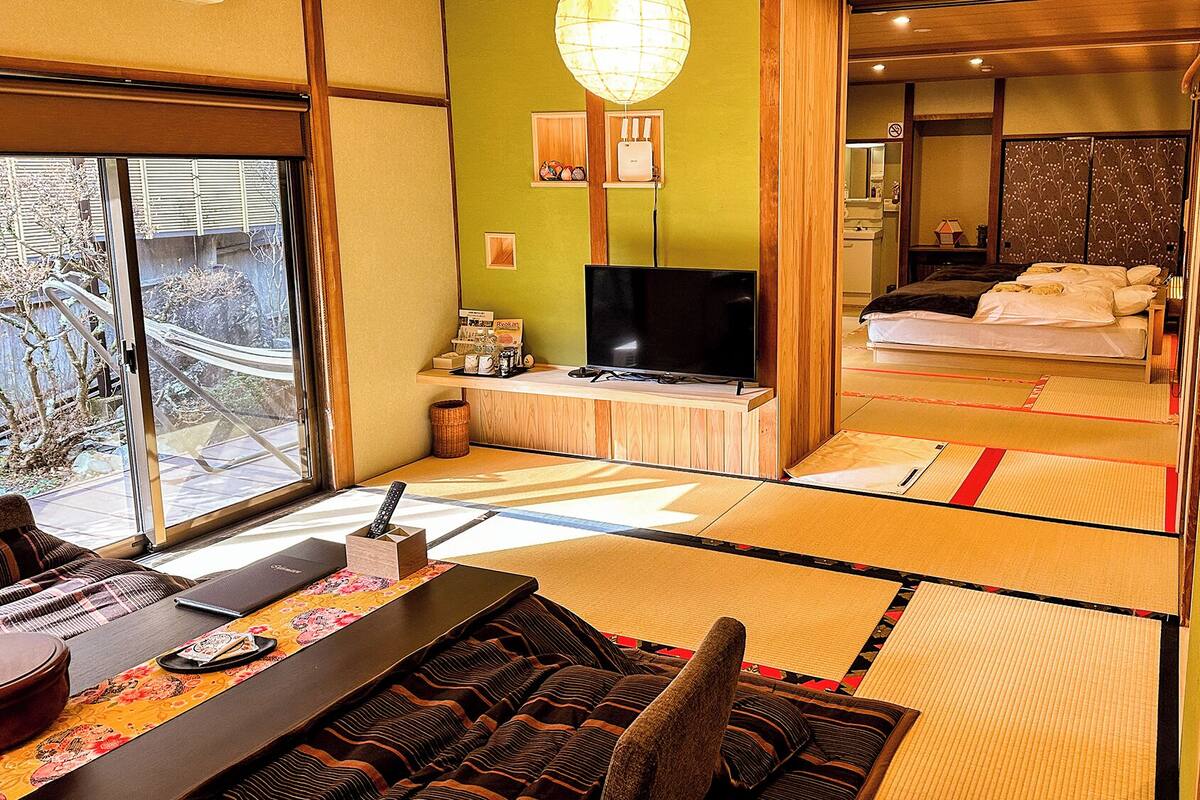 Quarto japonês tradicional com tatames, televisão, cama e vista para o exterior.