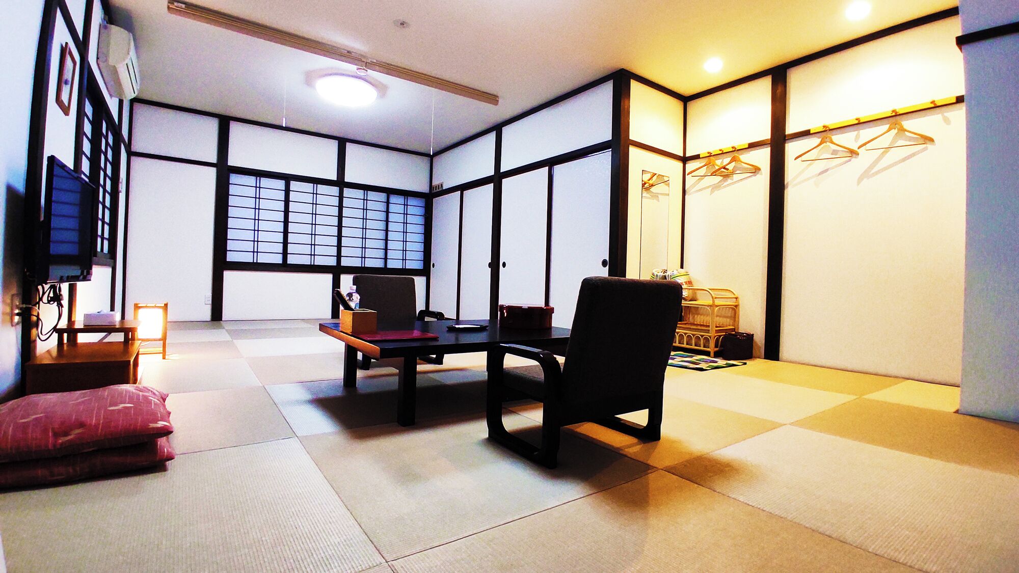 Une pièce de style japonais traditionnel, avec un sol recouvert de tatamis, une table basse, une chaise, un futon et une porte coulissante à motifs géométriques.