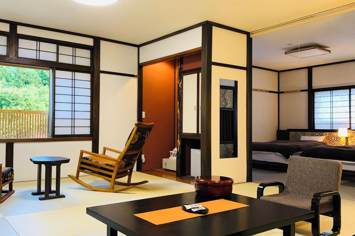 Une pièce de style japonais traditionnel, avec un sol recouvert de tatamis, une table basse, un fauteuil à bascule, un canapé et un lit doté d’une tête de lit à motifs.
