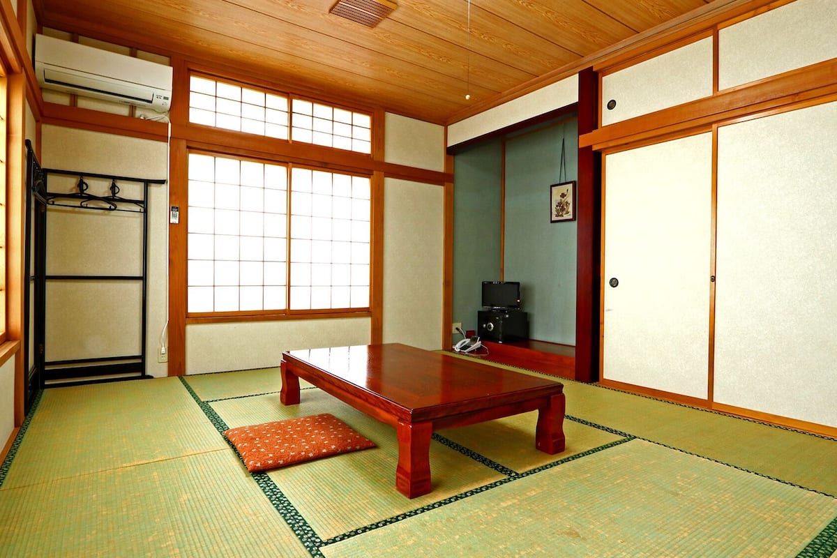 A traditional Japanese room with tatami flooring, a low wooden table, sliding doors, and a television.